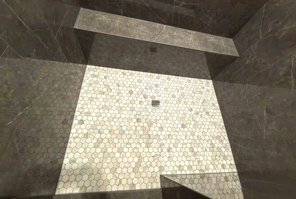 Marble hexagon mosaic floor pitched to a square drain