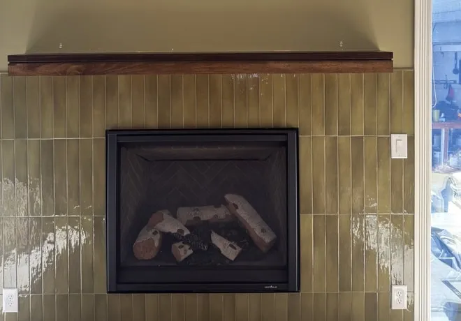 Fireplace with olive green vertical stacked tile and a dark wood mantel