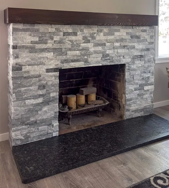 Stacked stone fireplace with a dark wood mantel and granite hearth